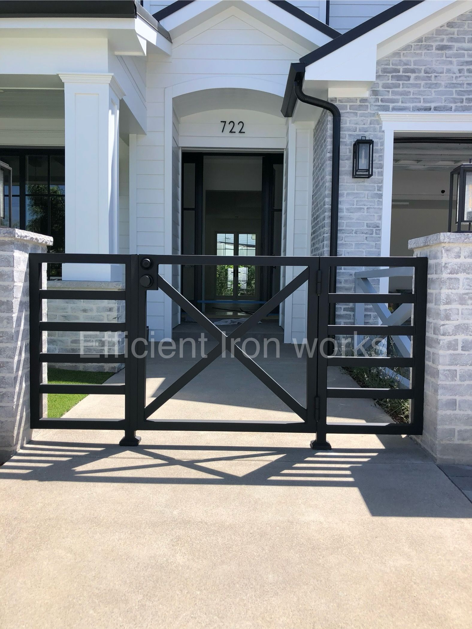 Black iron gate at the entrance of a white-columned house with a gray brick exterior. The gate is closed.