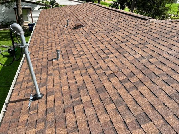 Brown shingle roof with several metal pipes and a mast extending upward.