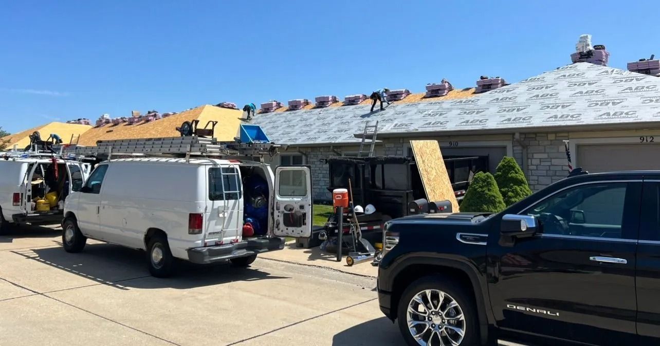 Roofers on a house roof replacing shingles. White vans and a black truck parked on the street.