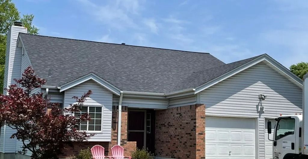 Grey roof on a light-colored house with a brick facade, white garage door, and a red tree.