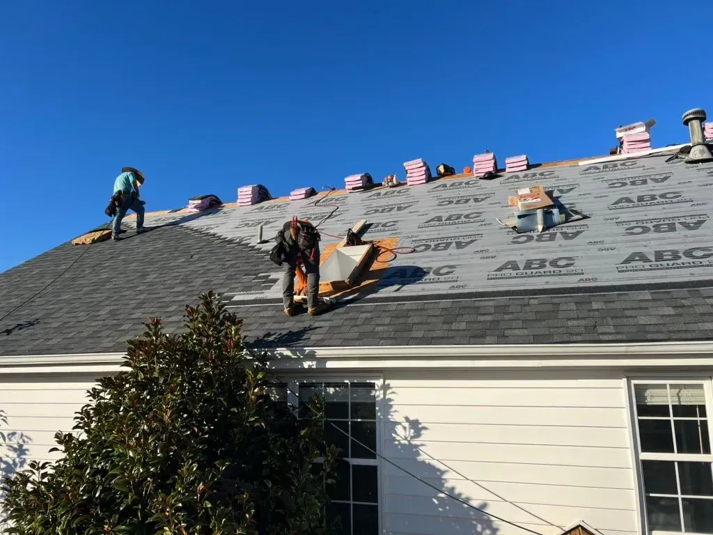 Roofers installing new shingles on a house under a clear, blue sky.