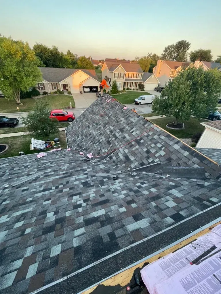 Roofer on a partially shingled roof with neighborhood homes in the background.