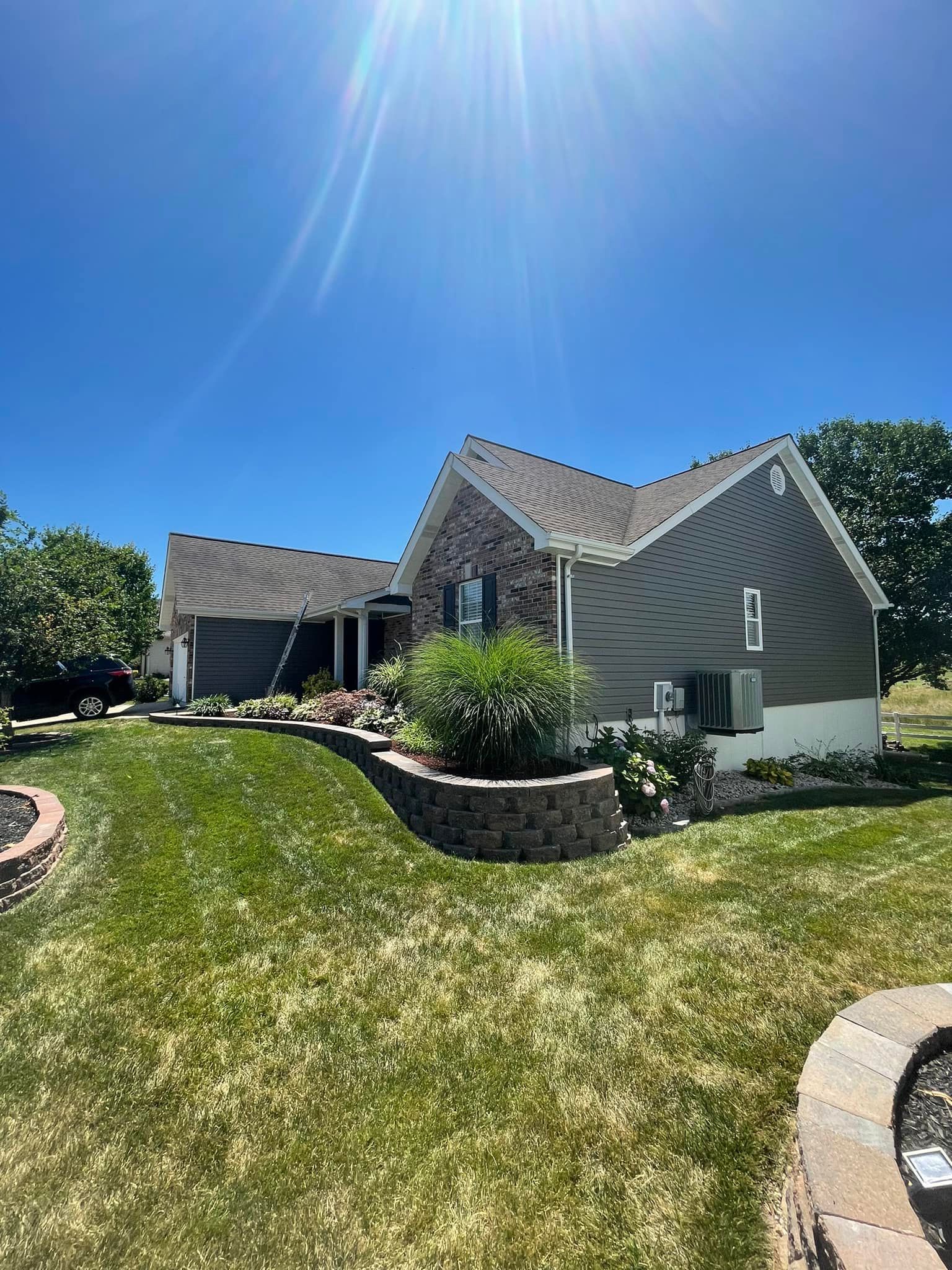 House with gray siding and brick accents on a sunny day. Green lawn and landscaping in the foreground.