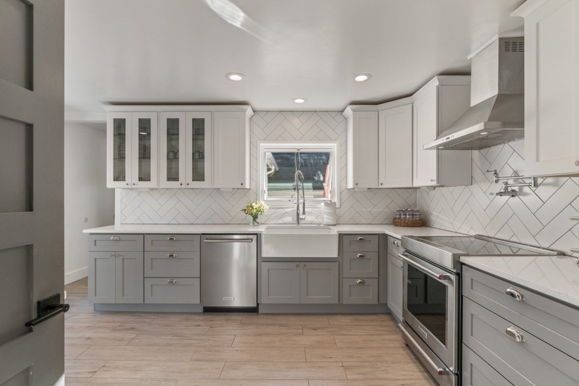 A kitchen with gray cabinets , white cabinets , stainless steel appliances , a sink and a window.