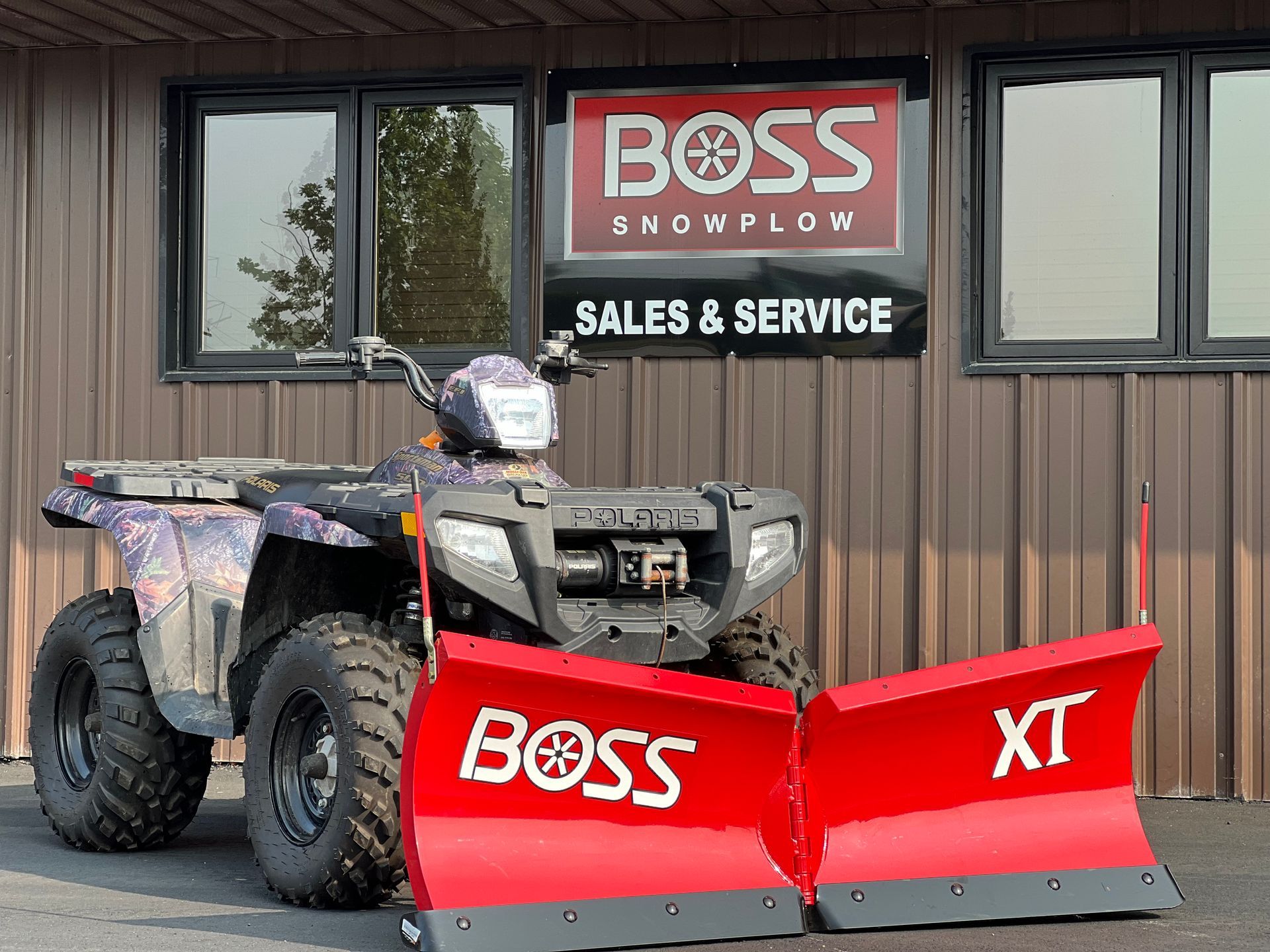 ATV with red BOSS snowplow parked outside a BOSS sales and service building