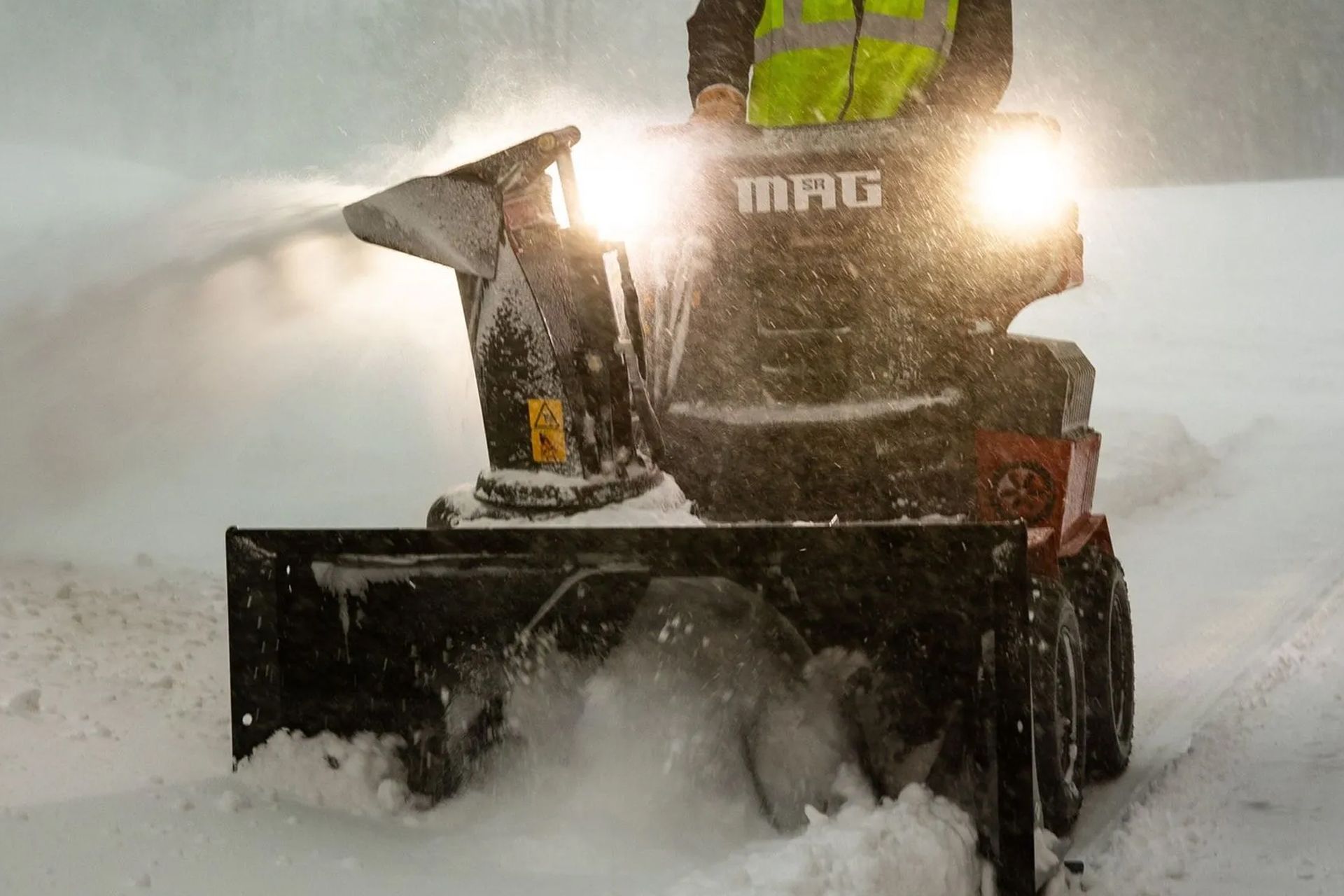 Snowblower clearing heavy snow in a snowy street, bright headlights glowing in the storm