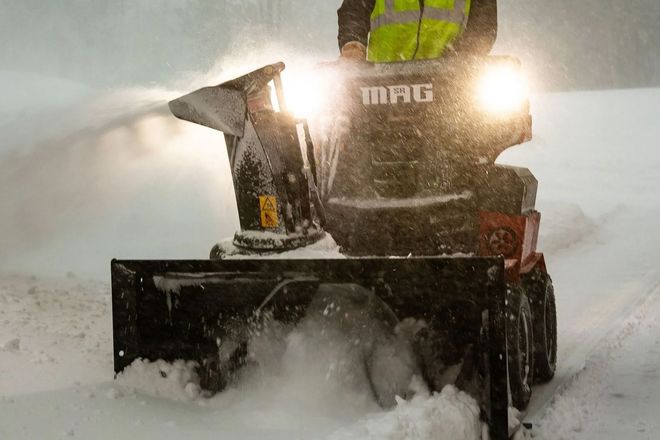 Snowblower clearing heavy snow in a snowy street, bright headlights glowing in the storm
