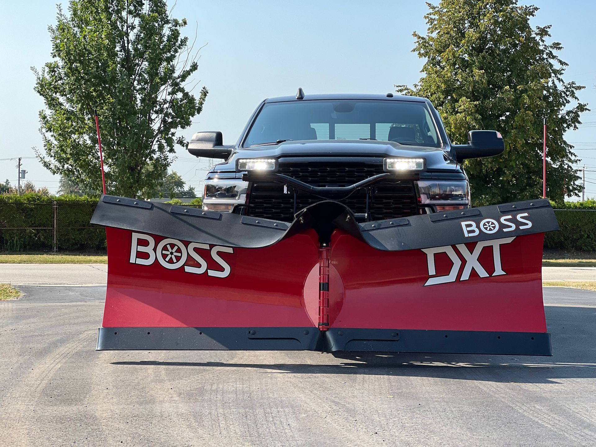 Black pickup truck with a red snow plow labeled BOSS on a sunny road.