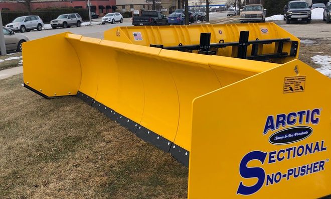 Yellow Arctic sectional snow pusher attachment sitting outdoors on grass