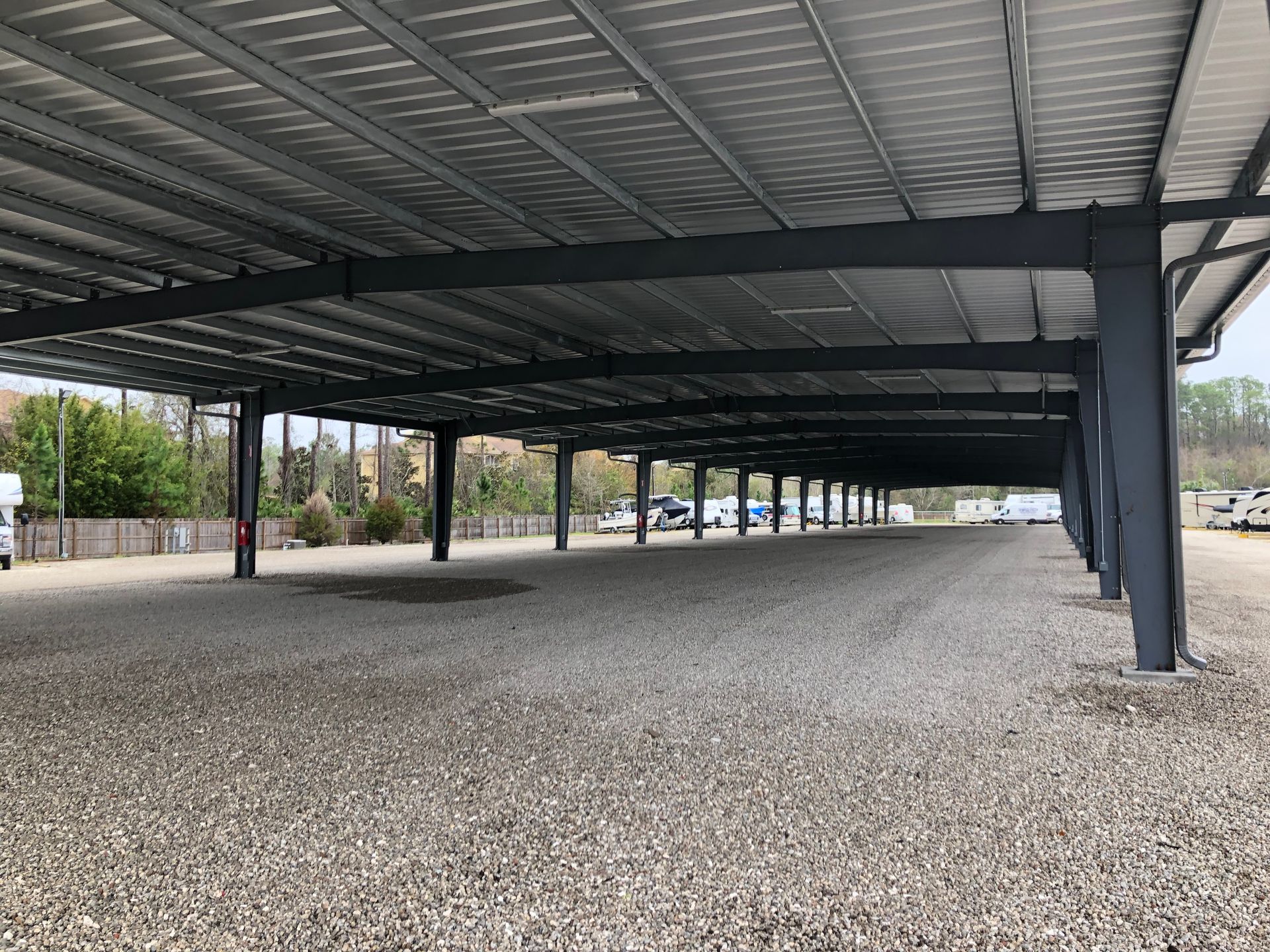 Empty covered gravel parking area with metal roof and support posts