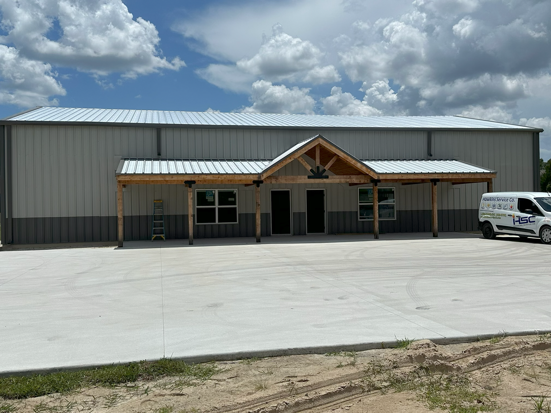 Front view of a gray metal building with a wooden entrance canopy and a white van parked beside it