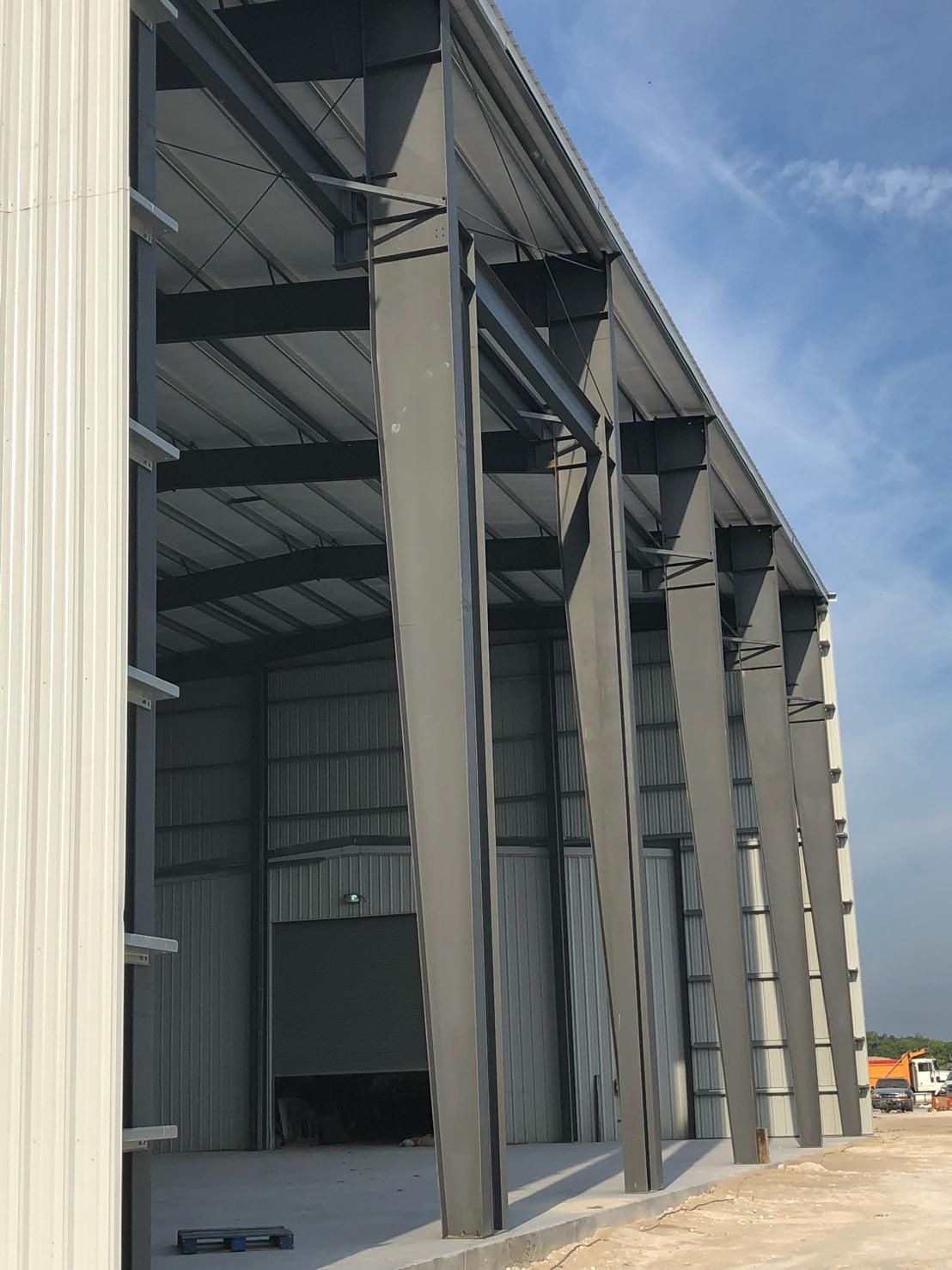 Large open-sided metal warehouse with steel beams under a blue sky