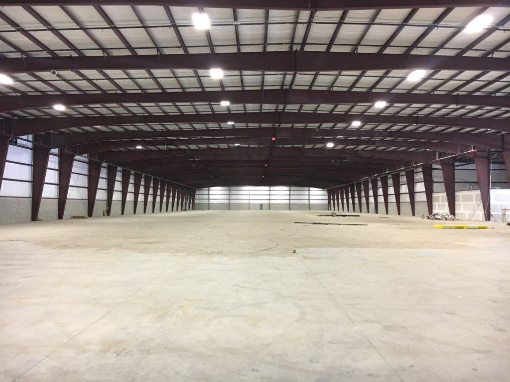 Large empty warehouse interior with steel beams, concrete floor, and bright overhead lights