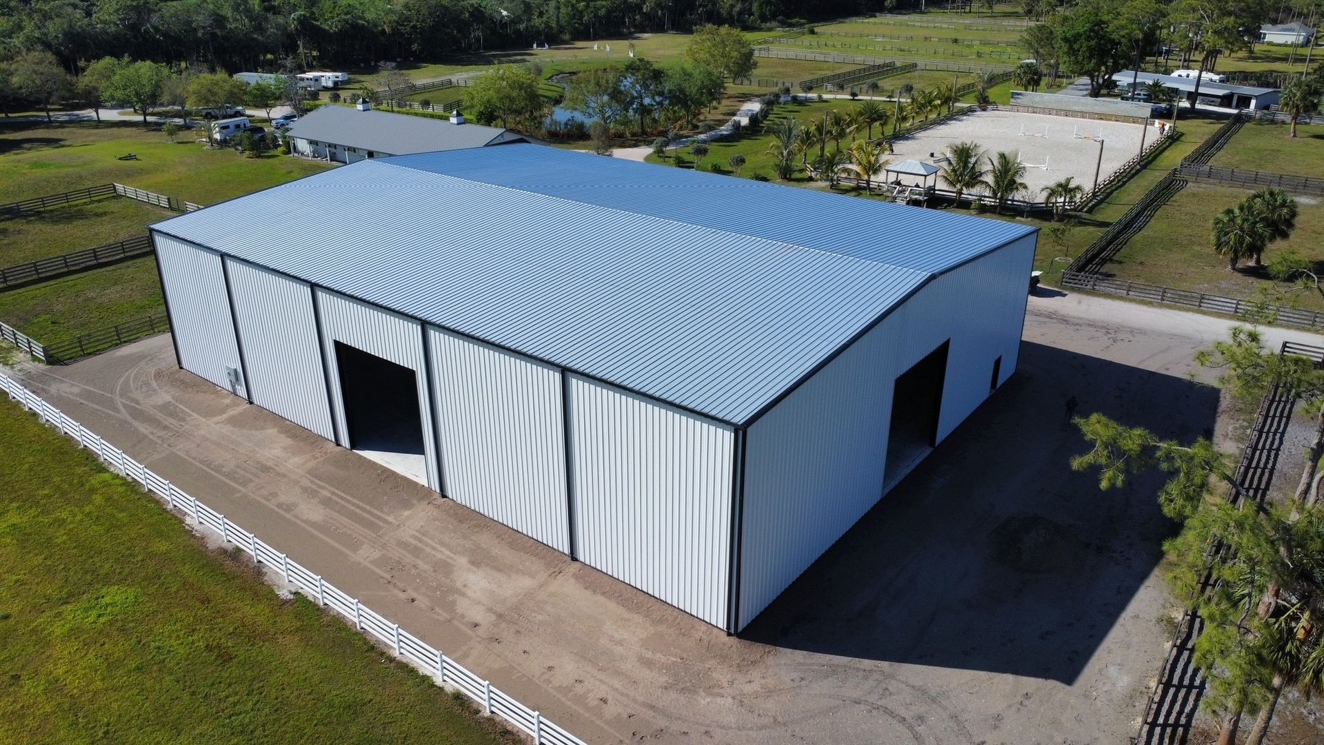 Aerial view of a large white metal warehouse with a blue roof in a rural area.