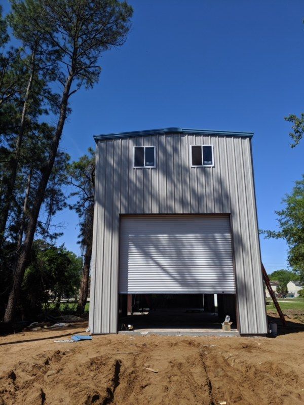 Small metal building with a roll-up door, viewed from the front on a dirt lot under a clear blue sky.