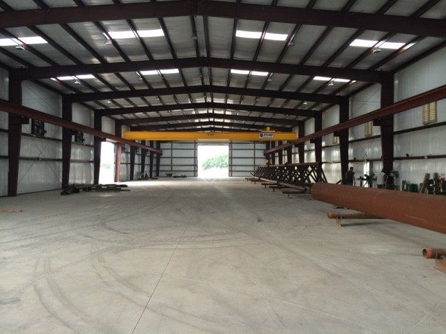 Empty industrial warehouse interior with steel beams, concrete floor, and open doors to daylight