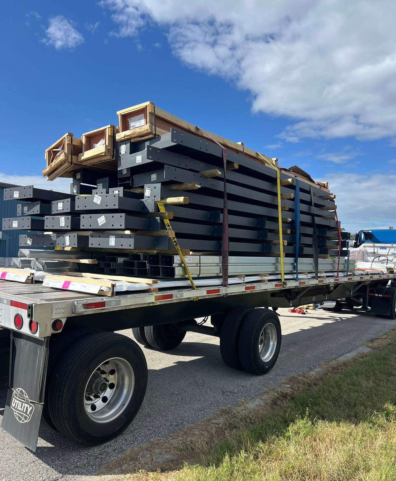 Flatbed trailer loaded with stacked black metal beams under a blue sky