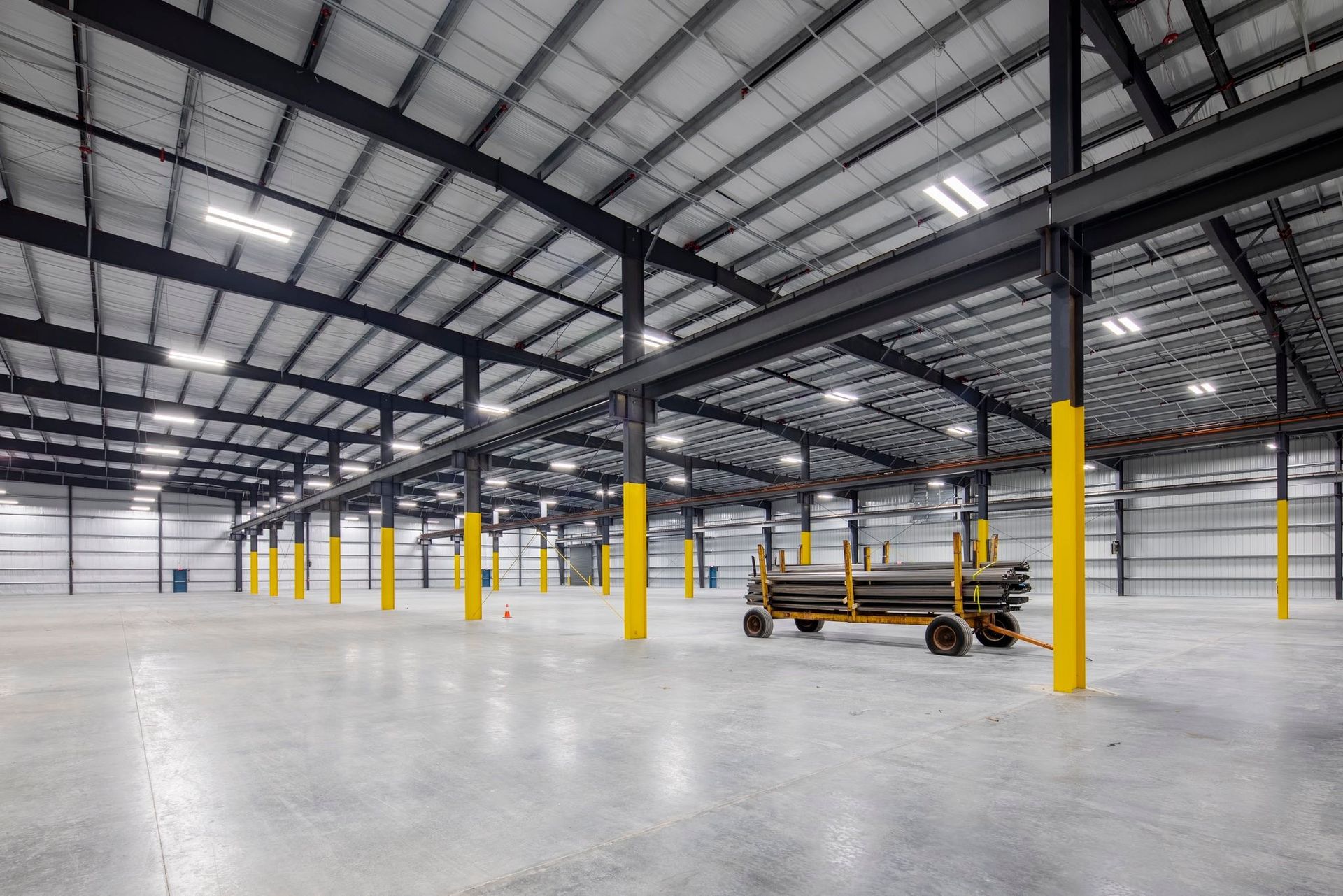 Empty industrial warehouse interior with yellow support columns and a forklift on a concrete floor