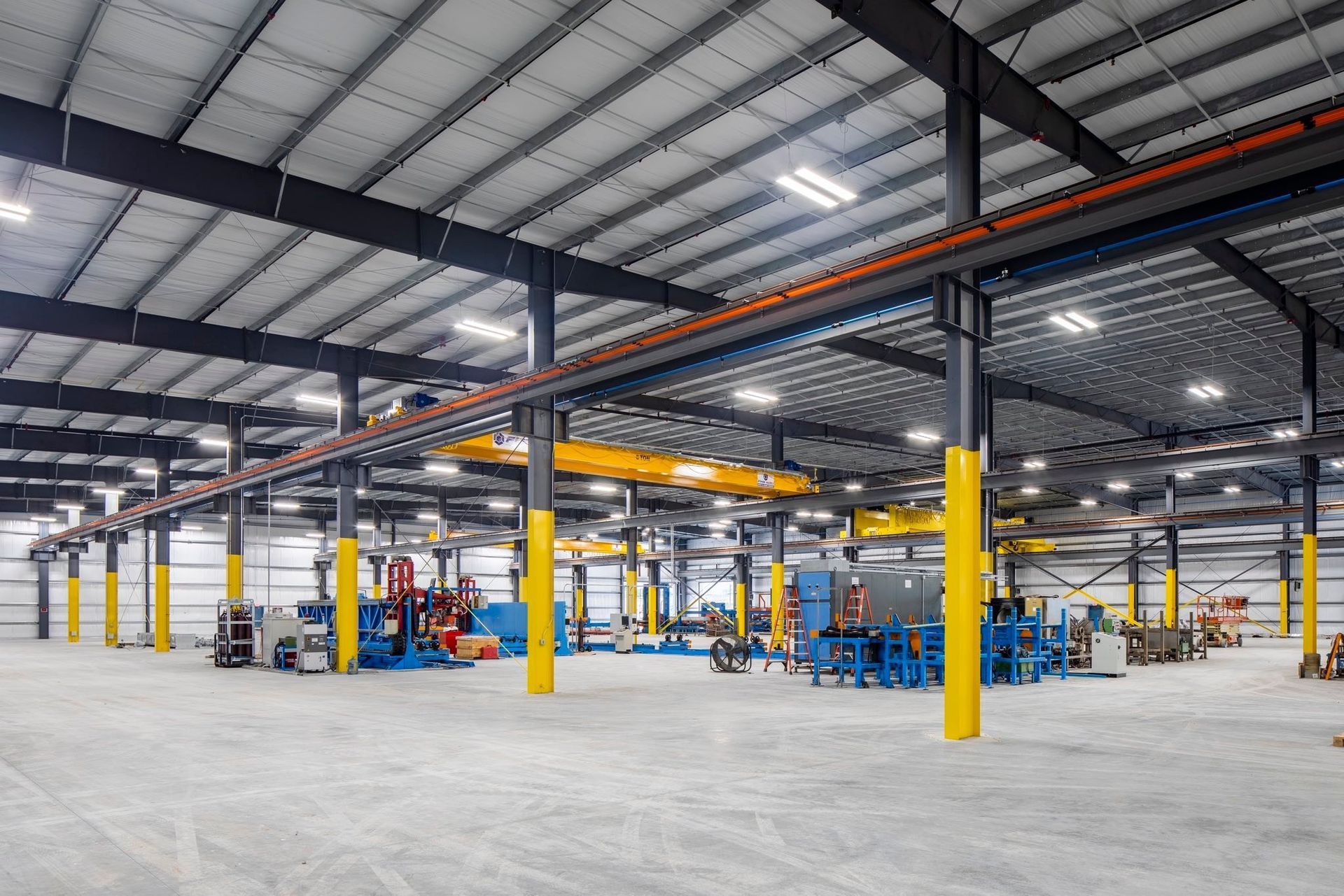 Spacious industrial warehouse with steel beams, yellow columns, and equipment on a concrete floor