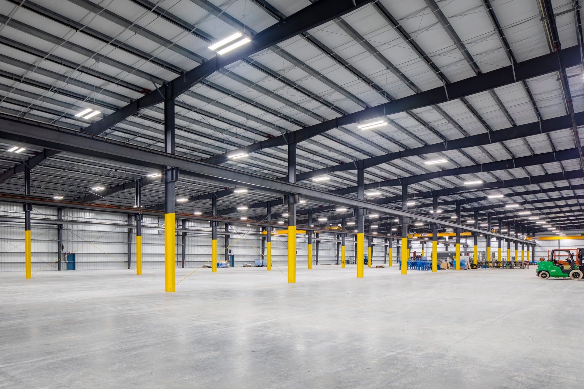 Empty warehouse interior with steel roof trusses, yellow columns, and polished concrete floor