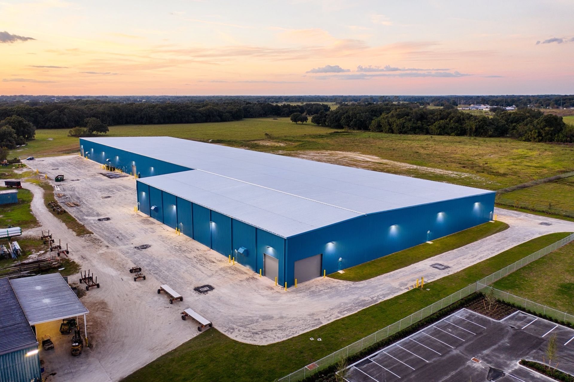 Aerial view of a large blue warehouse with white roof in an industrial area at sunset.