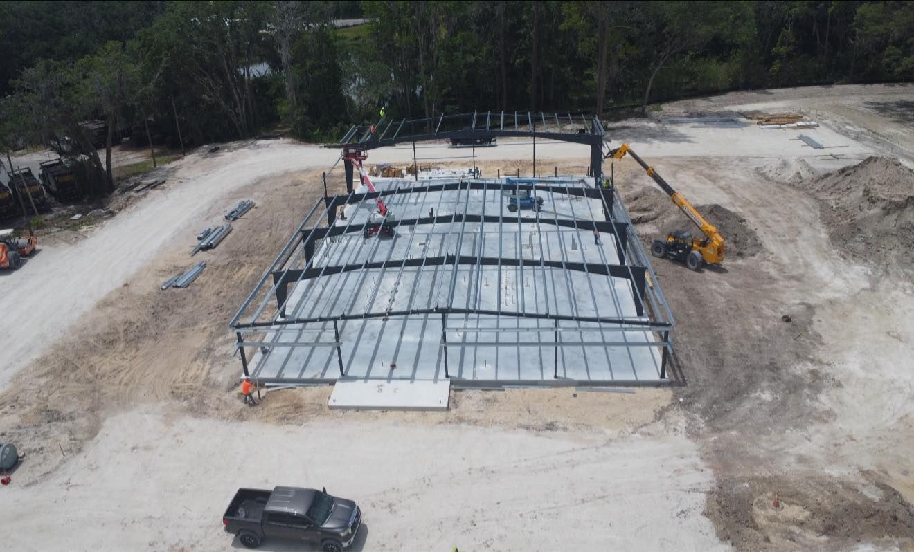 Aerial view of a steel-frame building under construction on a cleared site with machinery nearby