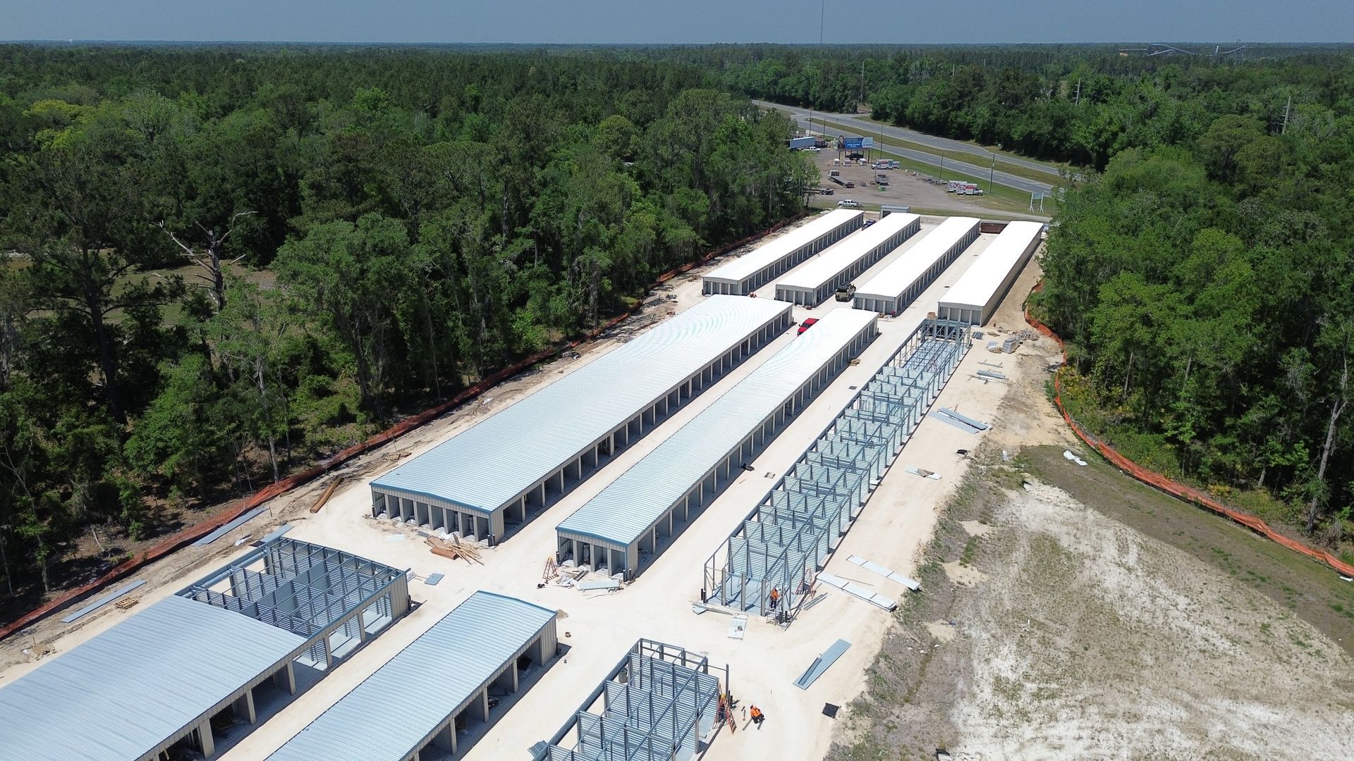 Aerial view of long white industrial buildings under construction beside dense green forest.