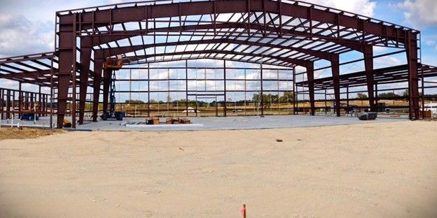Steel-framed building under construction on a sandy lot under a clear sky