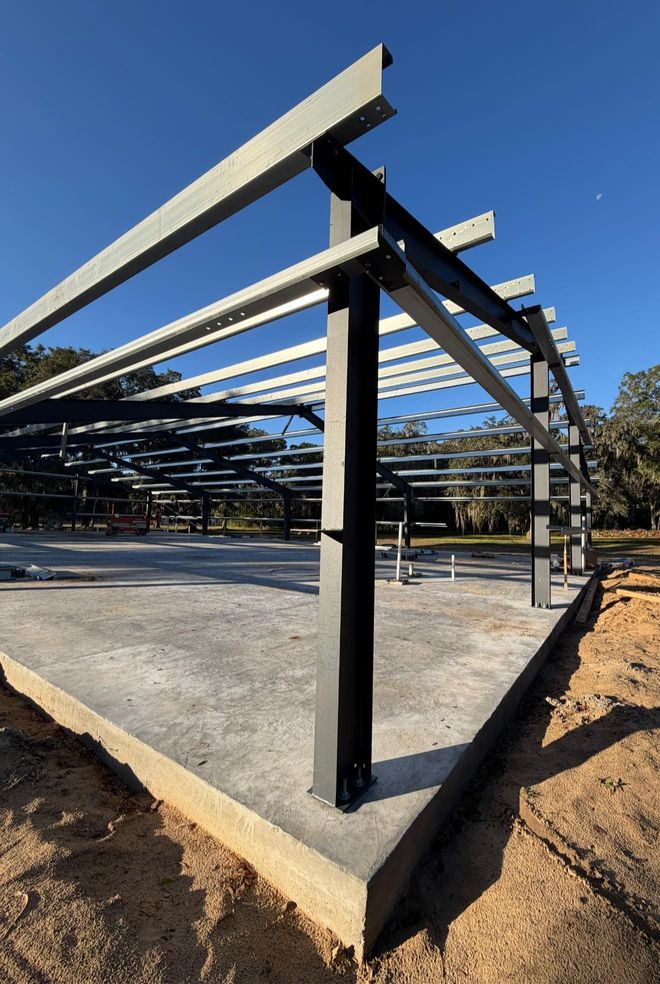 Steel-framed carport under construction on a concrete slab in a sunny outdoor lot