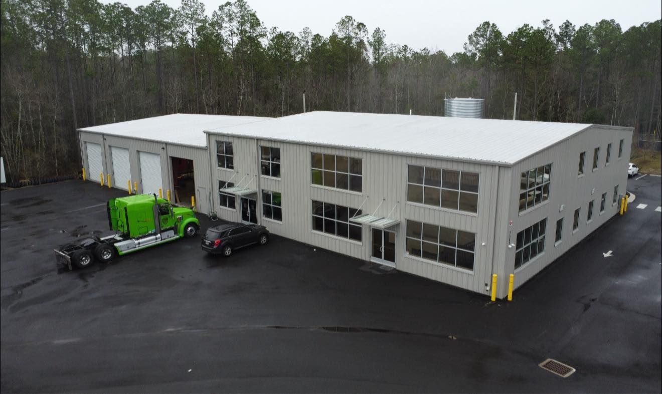 Industrial building with a white roof and green truck parked outside on a wet lot