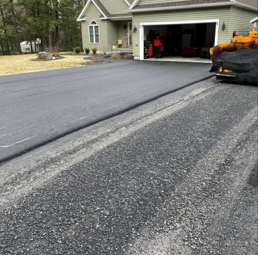 A newly paved, smooth black asphalt driveway leads to a suburban garage, contrasted by a coarse gravel section in the front.