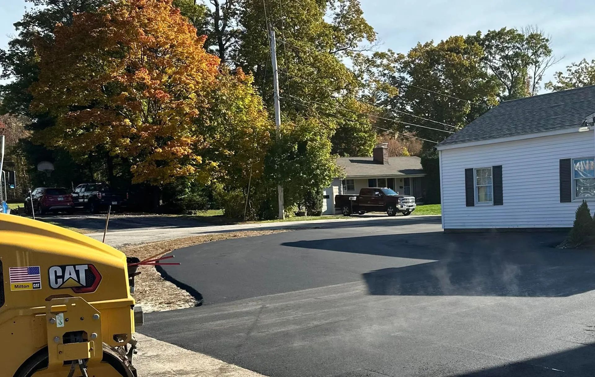 A yellow Caterpillar construction vehicle rests beside a freshly paved asphalt driveway in a residential yard.