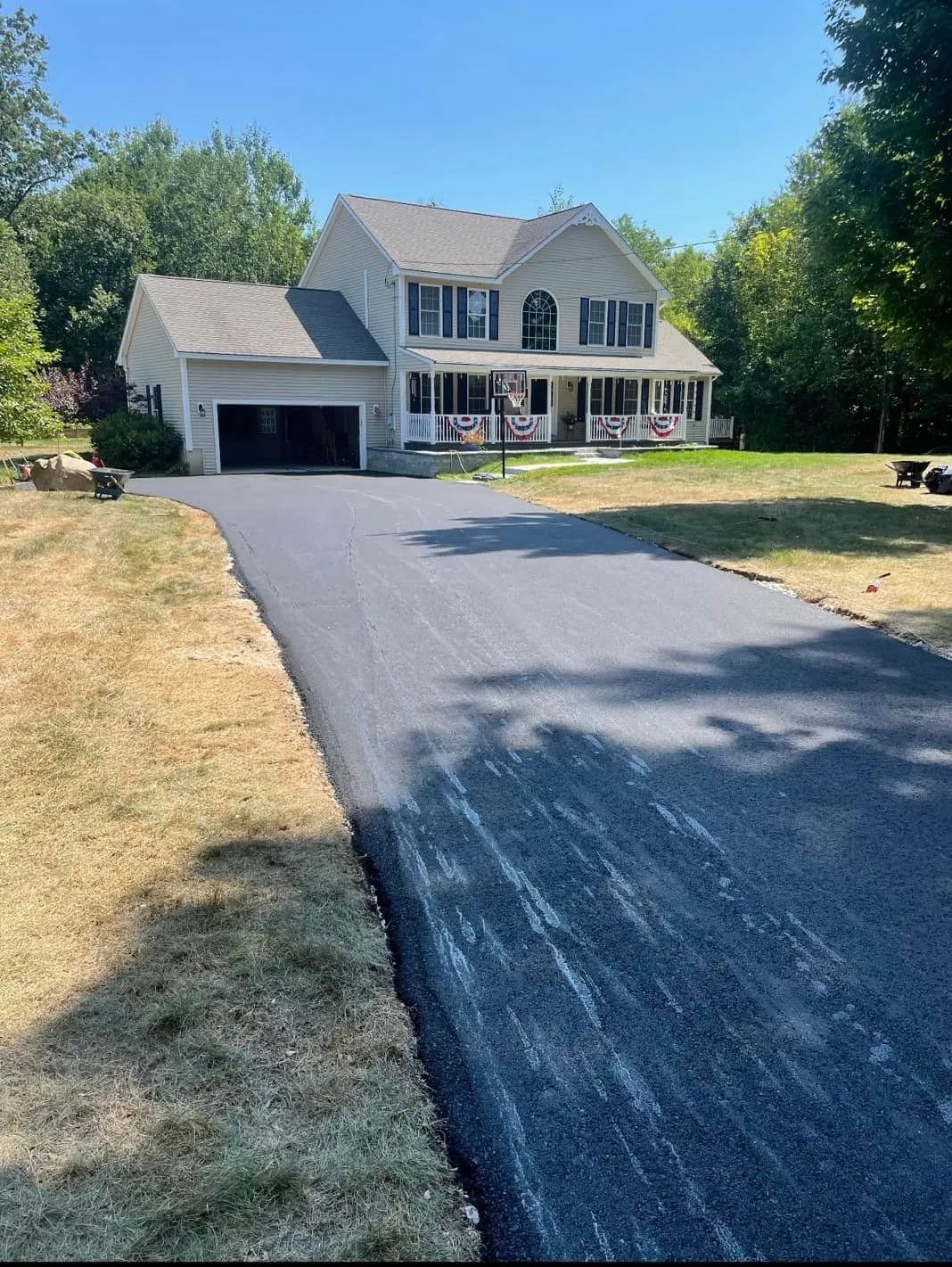 A two-story house with a white exterior and a freshly paved black asphalt driveway leading to a garage.