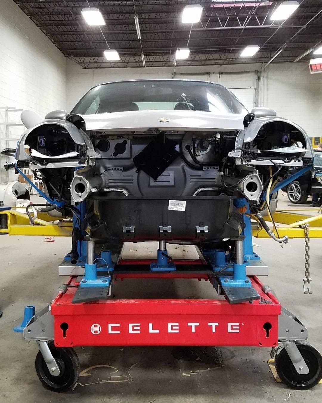 Front view of a car body on a red Celette frame in an auto repair shop, with front bumper removed