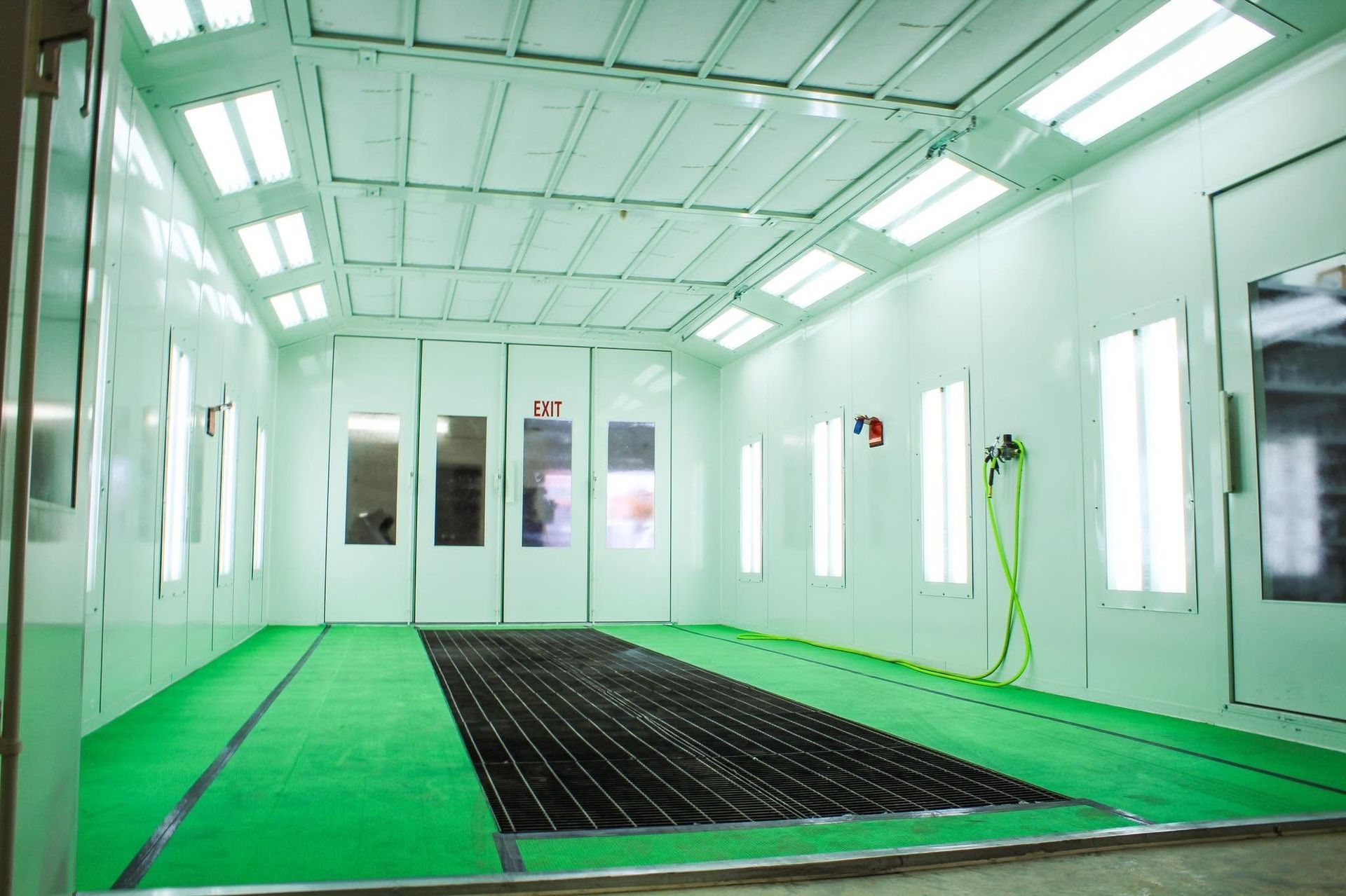 Empty mint-green spray booth with overhead lights and a black grated floor.