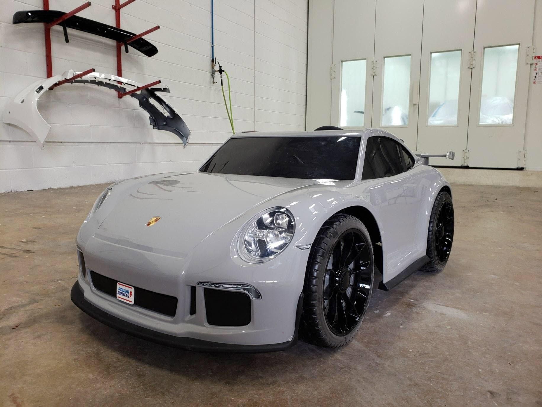 Gray sports car in a white garage, shown from the front-left with black wheels and tinted windows