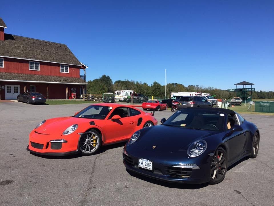 Two sports cars, red and black, parked on a sunny track with a red building in the background