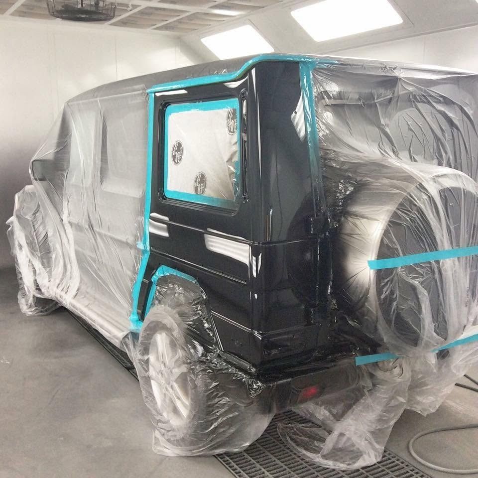 Black SUV wrapped in plastic and blue tape in a workshop, likely being prepped for painting