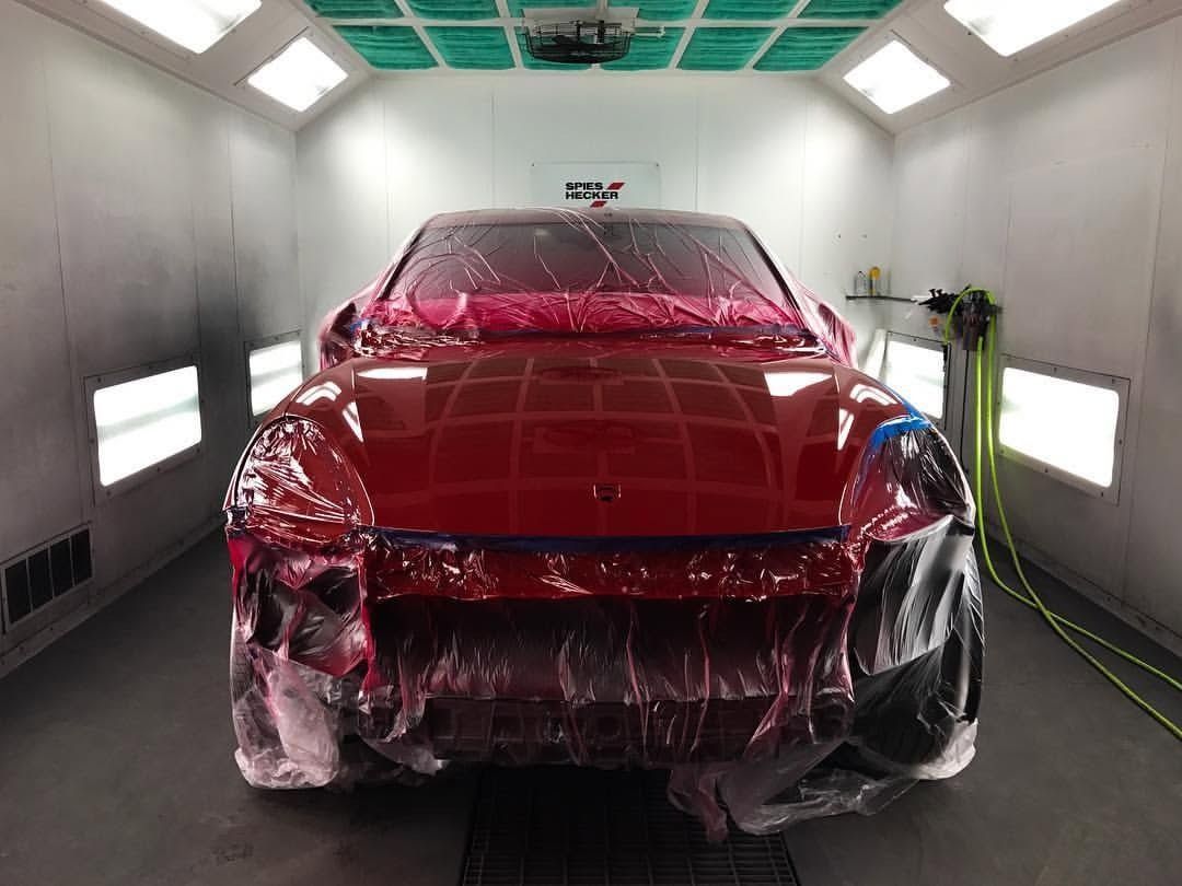 Red car wrapped in protective plastic inside a paint booth or detailing bay.