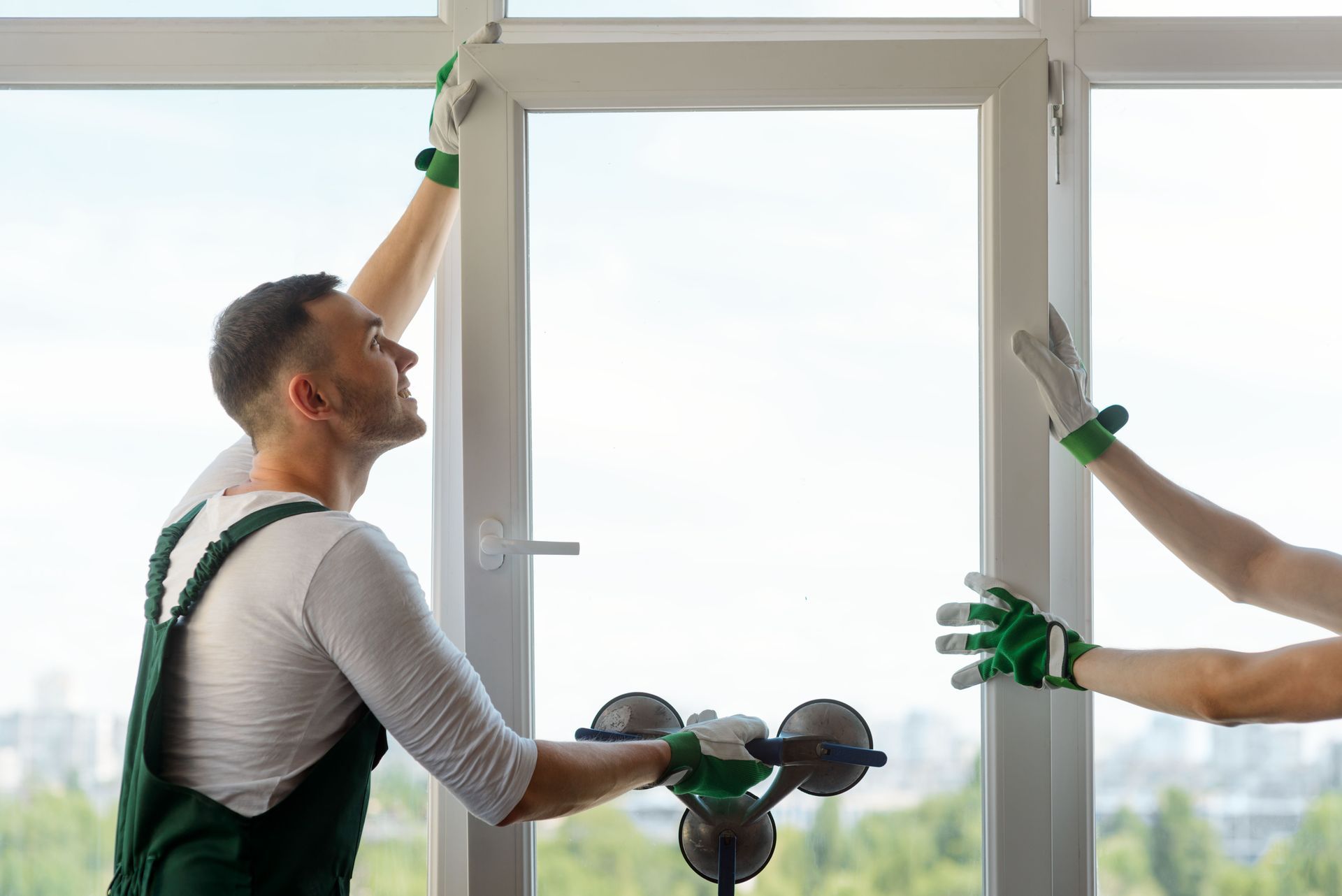 Two workers installing a white window frame indoors, one holding the top and one steadying the side