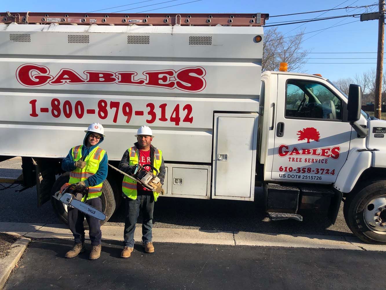 Two workers in hard hats and high-visibility vests stand smiling in front of a white 