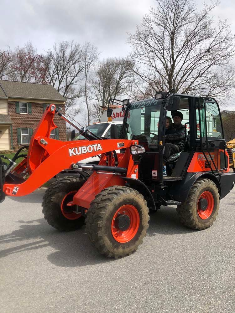 A bright orange Kubota wheel loader parked on an asphalt driveway in front of a residential house.