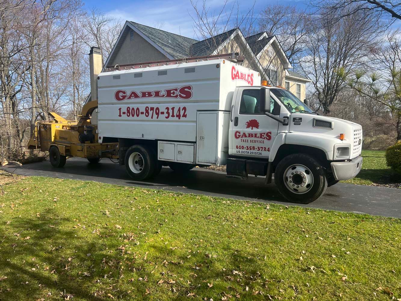 A white Gable's tree service truck with an attached wood chipper parked on a residential driveway.