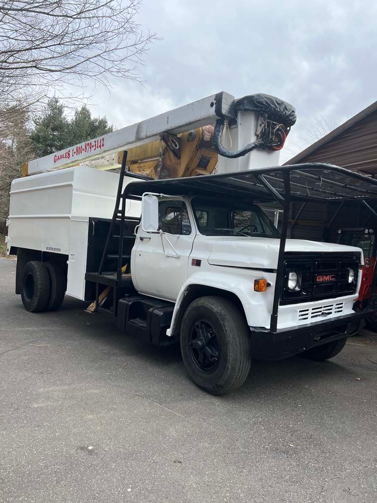 A white GMC bucket truck with a boom lift parked on asphalt, viewed from the front quarter angle.