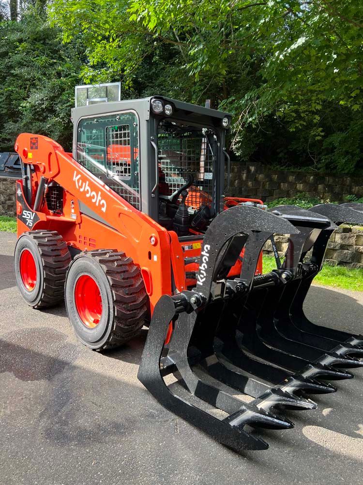 A bright orange Kubota skid steer loader with a black industrial grapple bucket attachment parked on an asphalt driveway.
