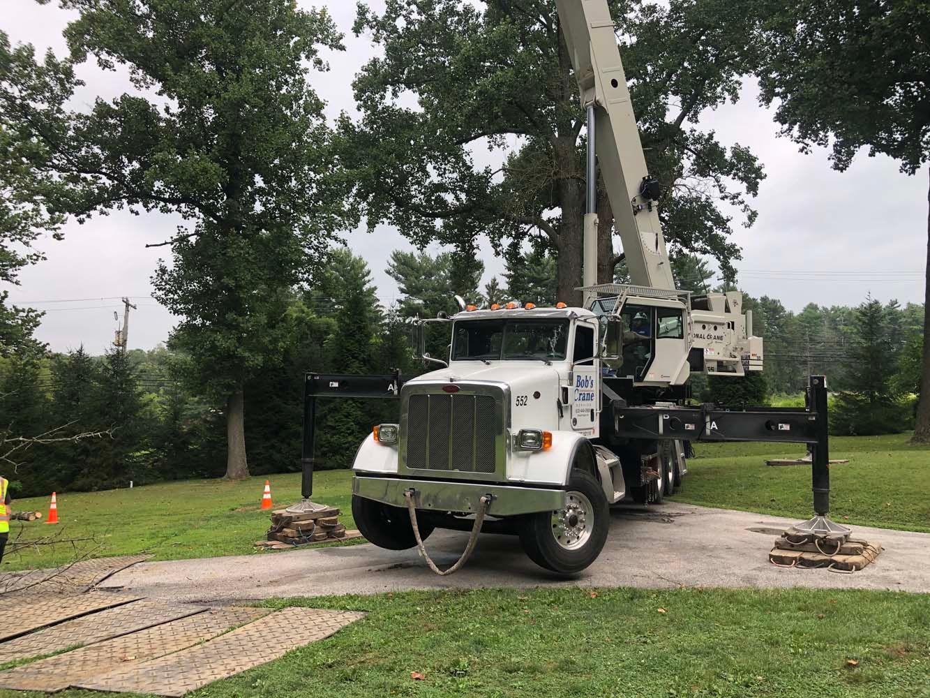 A white crane truck parked on a gravel area with extended outriggers stabilizing the vehicle on wooden pads.