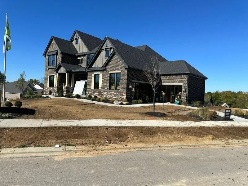 Large dark-gray house with stone accents on a bare lot beside a road under a clear blue sky