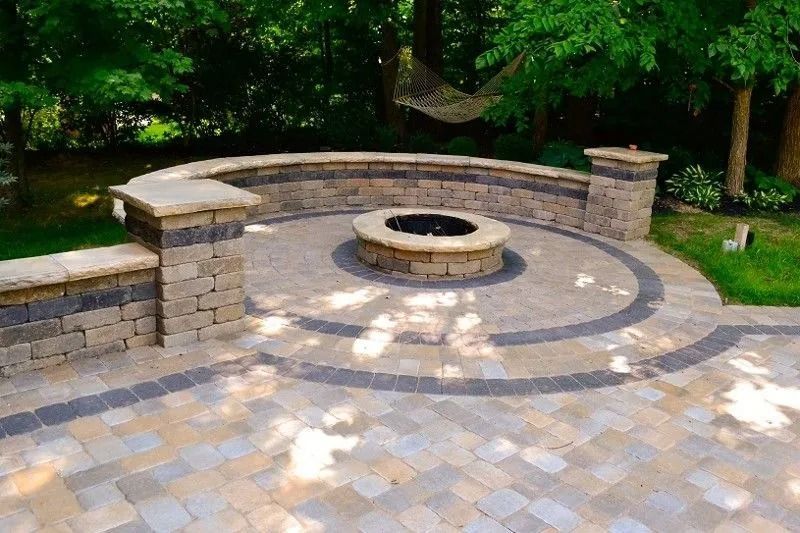 Stone patio with a circular fire pit and curved seating wall in a green wooded park