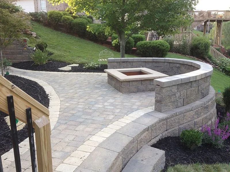 Curved stone patio with built-in seating and central fire pit in a landscaped garden