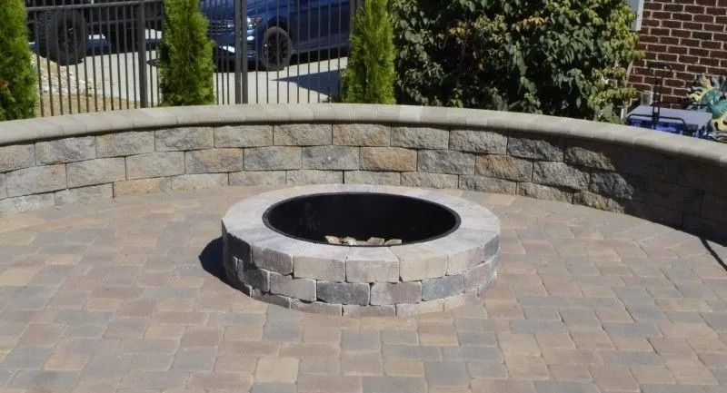 Stone fire pit in a paved patio with a curved stone wall backdrop.
